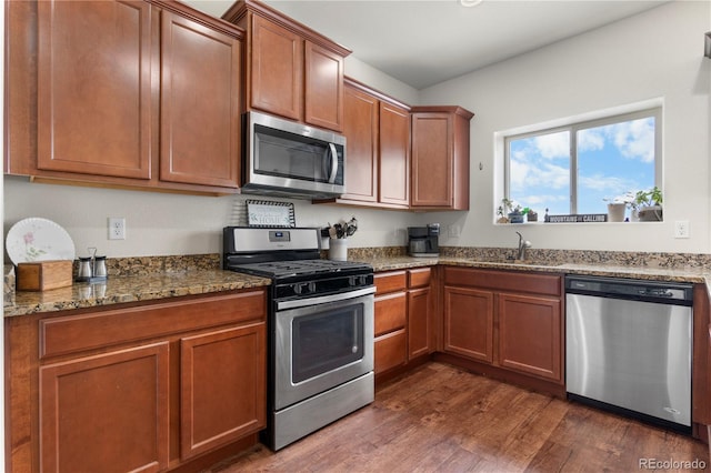 kitchen with appliances with stainless steel finishes, dark hardwood / wood-style flooring, sink, and stone counters