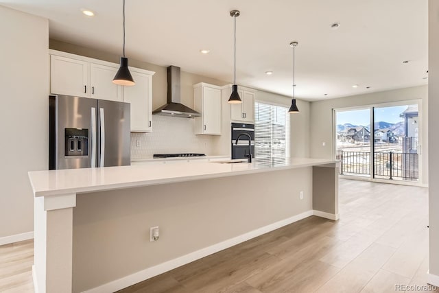 kitchen featuring stainless steel refrigerator with ice dispenser, sink, wall chimney range hood, a large island, and white cabinets