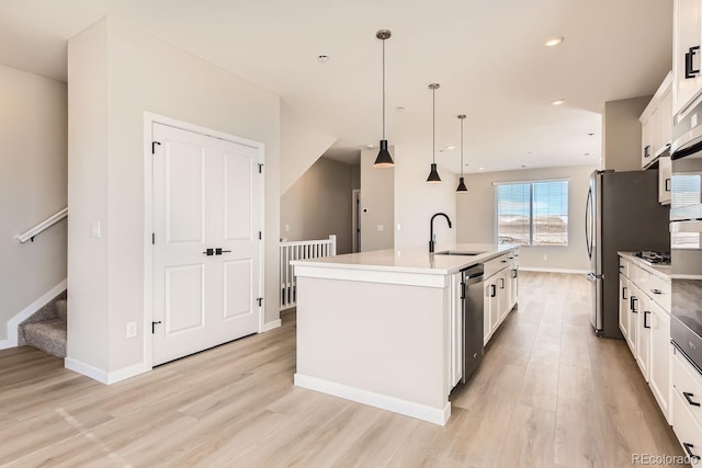 kitchen featuring sink, appliances with stainless steel finishes, hanging light fixtures, white cabinets, and a center island with sink