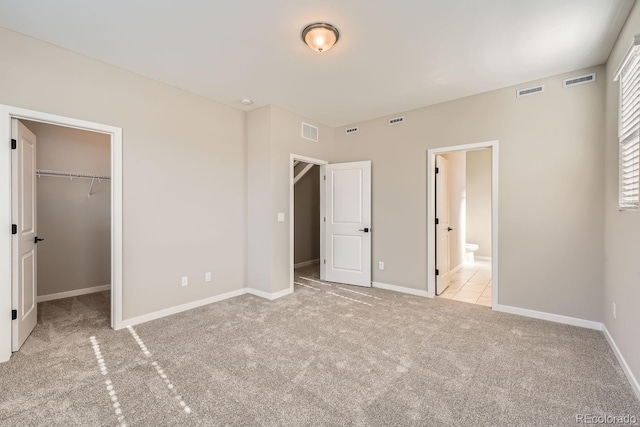 unfurnished bedroom with light colored carpet, connected bathroom, a closet, and a walk in closet