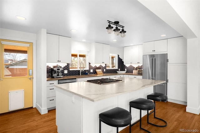 3925 Newland St, Wheat Ridge, CO 80033 - kitchen with stainless steel appliances, a center island, a kitchen breakfast bar, decorative backsplash, and recessed lighting