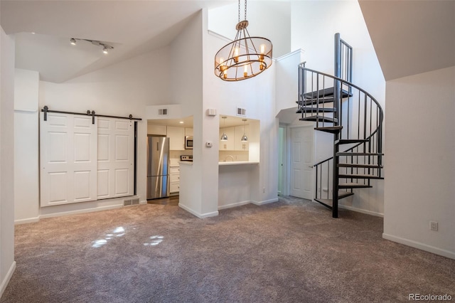 4943 S Carson St Unit 207, Aurora, CO 80015 - unfurnished living room featuring carpet flooring, a barn door, a chandelier, stairway, and high vaulted ceiling