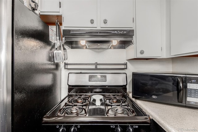 kitchen featuring stainless steel gas range, freestanding refrigerator, white cabinets, and exhaust hood