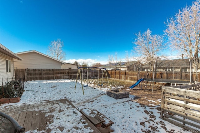 yard covered in snow featuring a trampoline, a playground, and a fenced backyard