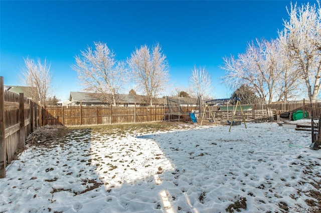 yard covered in snow with a trampoline, a playground, and a fenced backyard