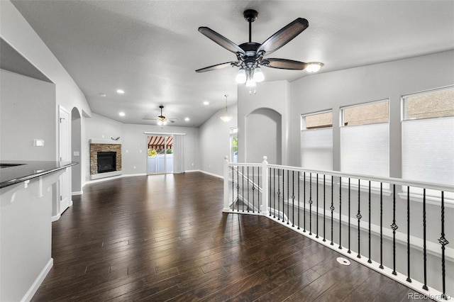 unfurnished living room with a stone fireplace, a textured ceiling, vaulted ceiling, dark wood-type flooring, and ceiling fan