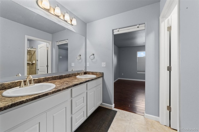 bathroom with baseboards, double vanity, a sink, and tile patterned floors