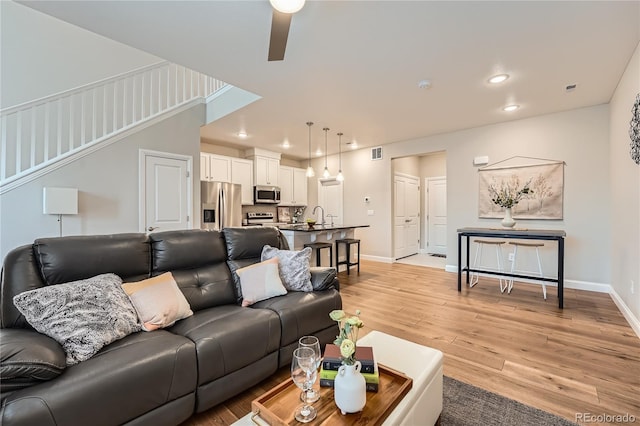 living room featuring sink, ceiling fan, and light wood-type flooring