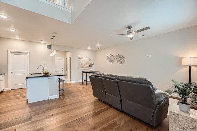 living room featuring ceiling fan, sink, and light wood-type flooring