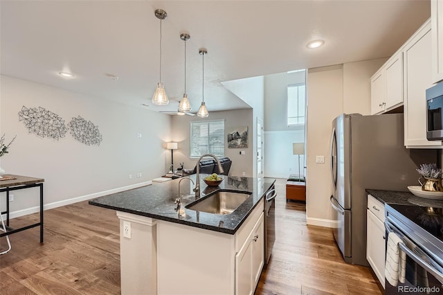 kitchen with an island with sink, decorative light fixtures, sink, and white cabinets