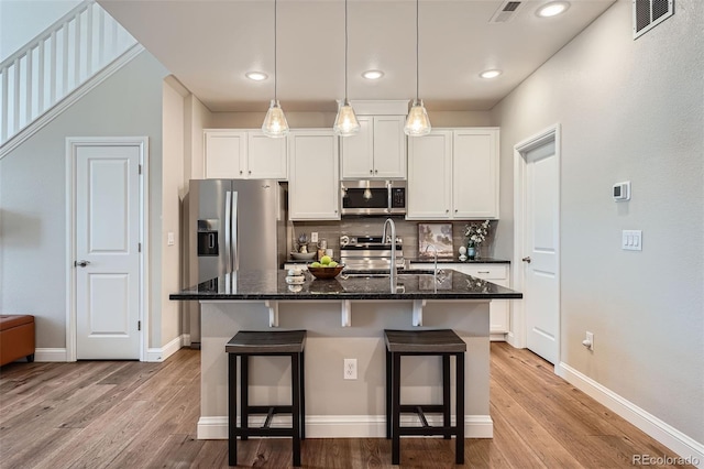 kitchen featuring a kitchen bar, a center island with sink, appliances with stainless steel finishes, dark stone counters, and white cabinets