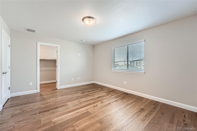 unfurnished bedroom with a closet, a spacious closet, light hardwood / wood-style flooring, and a textured ceiling