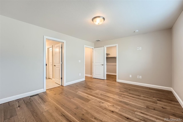 unfurnished bedroom featuring hardwood / wood-style flooring, a spacious closet, connected bathroom, and a closet