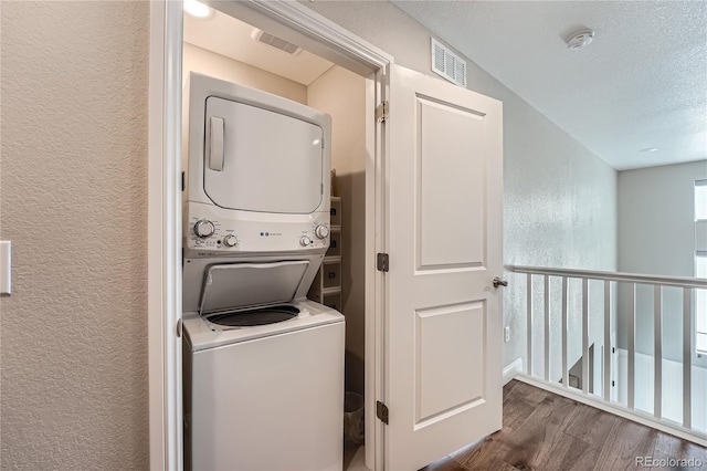 clothes washing area with dark hardwood / wood-style floors, stacked washer and clothes dryer, and a textured ceiling