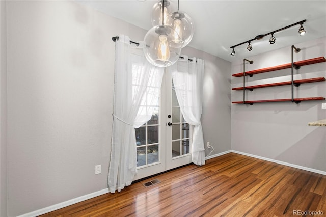 unfurnished dining area featuring wood-type flooring, track lighting, and french doors