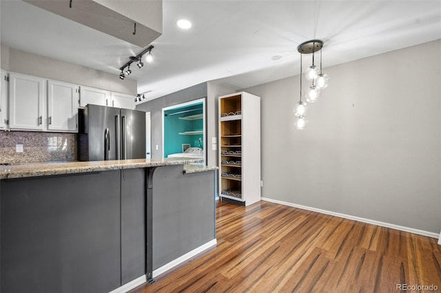 kitchen featuring hanging light fixtures, decorative backsplash, stainless steel fridge, dark hardwood / wood-style floors, and white cabinetry