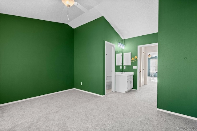 unfurnished bedroom with lofted ceiling, ensuite bath, ceiling fan, a textured ceiling, and light colored carpet