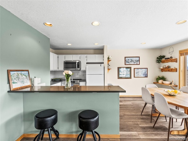 kitchen with a breakfast bar area, appliances with stainless steel finishes, white cabinets, kitchen peninsula, and light wood-type flooring