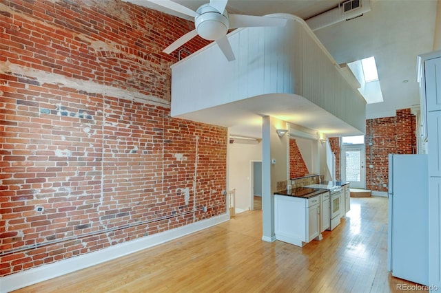 kitchen featuring white appliances, ceiling fan, high vaulted ceiling, light hardwood / wood-style floors, and brick wall