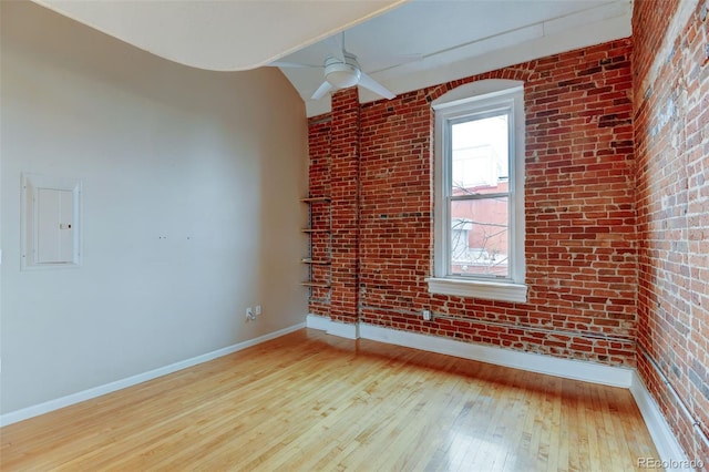 unfurnished room featuring ceiling fan, brick wall, electric panel, and light hardwood / wood-style floors