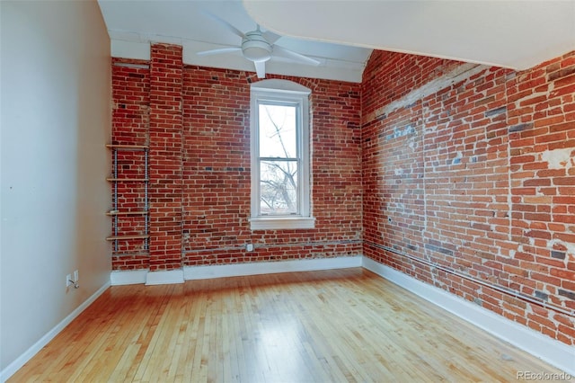 unfurnished room featuring ceiling fan, brick wall, and light wood-type flooring