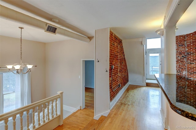 hallway featuring brick wall, light hardwood / wood-style flooring, and a notable chandelier