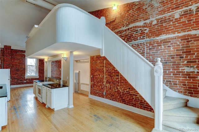 kitchen featuring white range with electric cooktop, brick wall, light wood-type flooring, and a towering ceiling