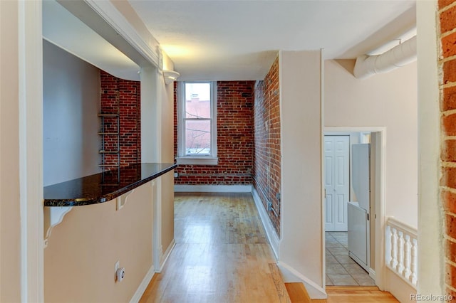 corridor featuring brick wall and light hardwood / wood-style flooring