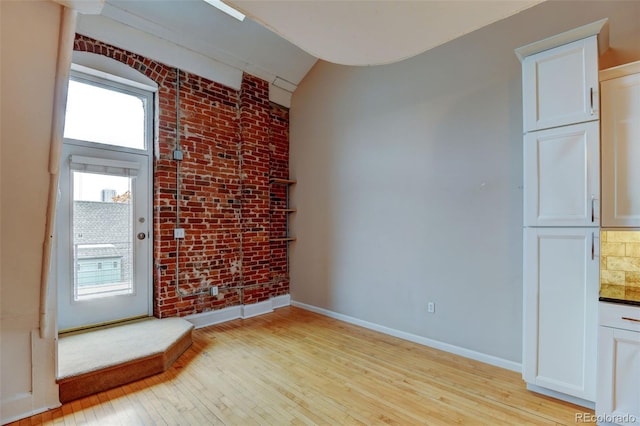 spare room with light hardwood / wood-style flooring and brick wall