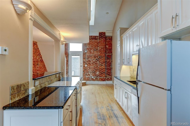 kitchen with brick wall, white cabinets, dark stone counters, white appliances, and light hardwood / wood-style flooring