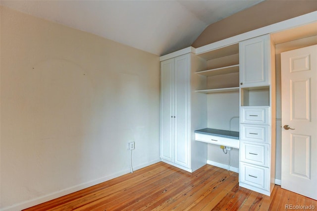 unfurnished bedroom featuring lofted ceiling, built in desk, and light hardwood / wood-style flooring