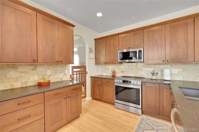 20530 Parker Vista Cir, Parker, CO 80138 - kitchen featuring appliances with stainless steel finishes, dark countertops, arched walkways, tasteful backsplash, and light wood-style floors