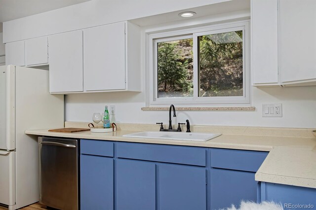 kitchen with light countertops, a sink, freestanding refrigerator, white cabinetry, and blue cabinetry