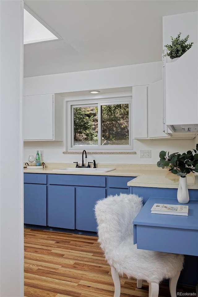 kitchen featuring light countertops, a sink, white cabinets, light wood-style floors, and blue cabinetry