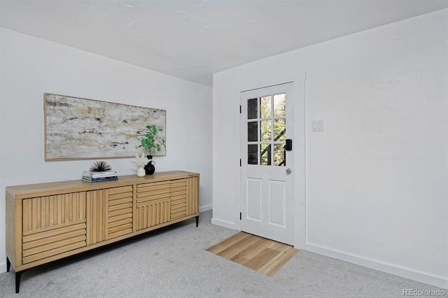 foyer featuring baseboards and light colored carpet