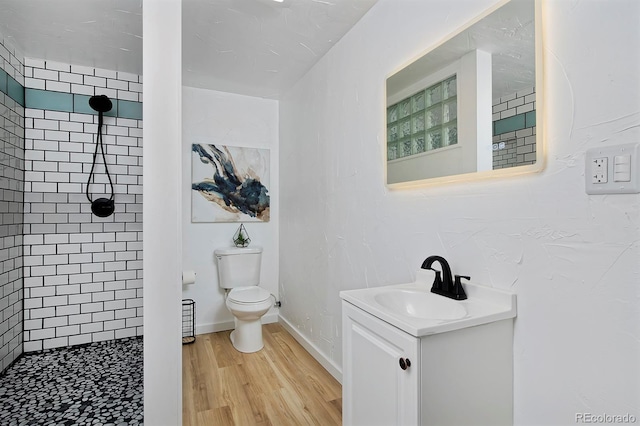 bathroom with toilet, tiled shower, vanity, wood finished floors, and baseboards