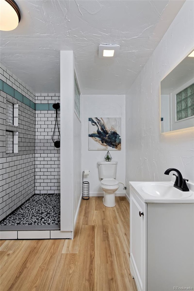 bathroom with a tile shower, toilet, vanity, wood finished floors, and baseboards