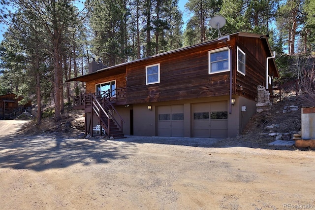 rustic home with driveway, a chimney, a garage, and stairway
