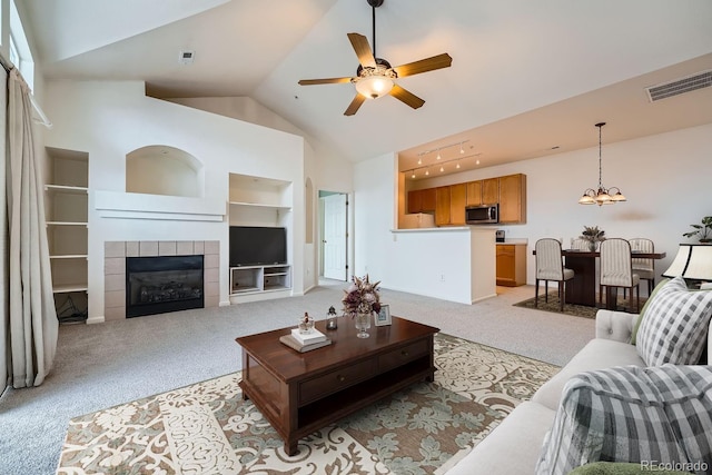 living room featuring high vaulted ceiling, built in shelves, a tile fireplace, light carpet, and visible vents