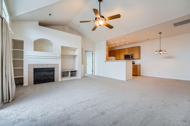 unfurnished living room with ceiling fan with notable chandelier, a fireplace, high vaulted ceiling, and light colored carpet