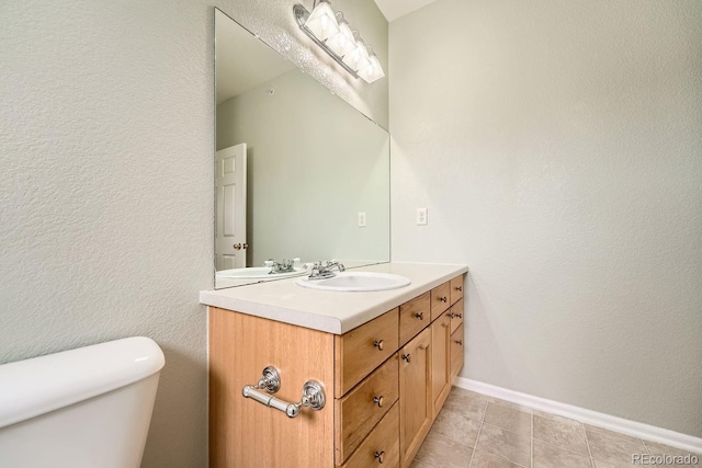 bathroom featuring baseboards, a textured wall, toilet, tile patterned flooring, and vanity