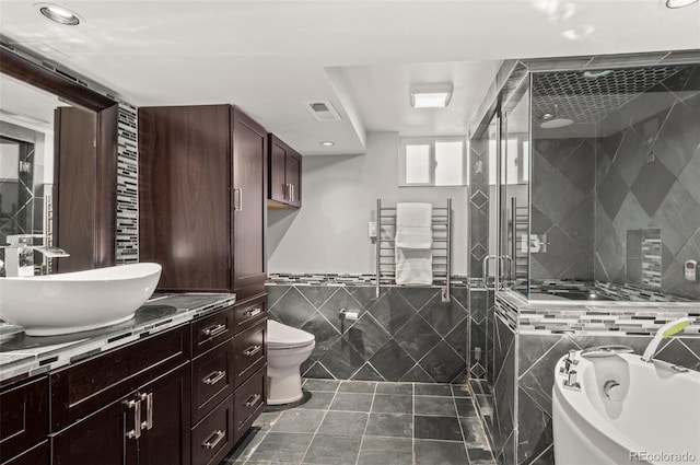 full bathroom with radiator heating unit, independent shower and bath, tile walls, vanity, and toilet