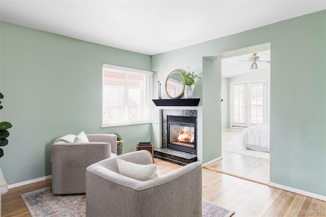 living area with a high end fireplace, vaulted ceiling, baseboards, and wood finished floors