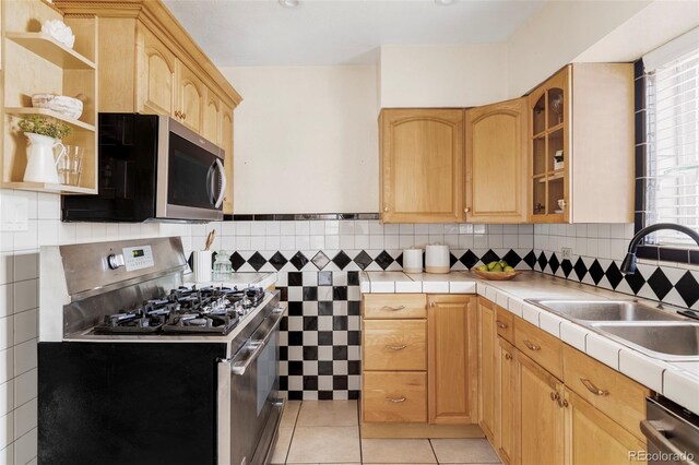 kitchen featuring light brown cabinetry, a sink, tile countertops, appliances with stainless steel finishes, and light tile patterned floors