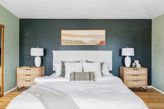 bedroom with an accent wall, baseboards, and wood finished floors