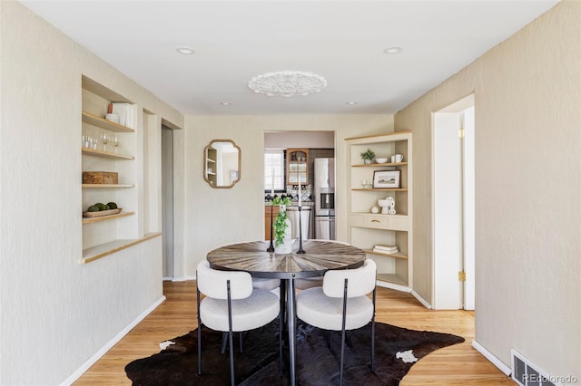 dining space with light wood-style flooring, built in features, baseboards, and visible vents