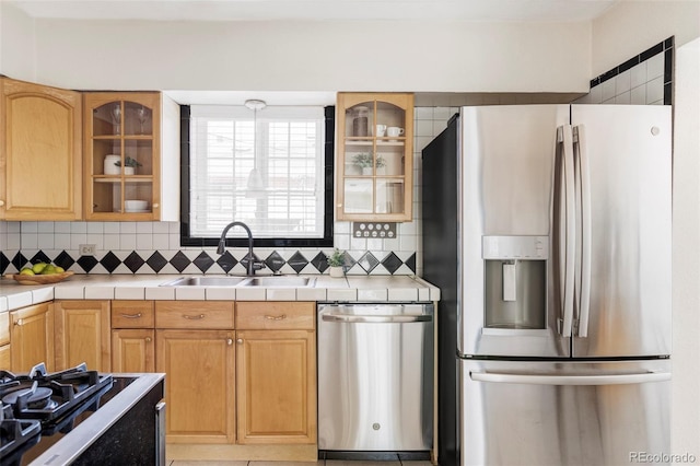 kitchen featuring stainless steel appliances, a sink, tile counters, and backsplash