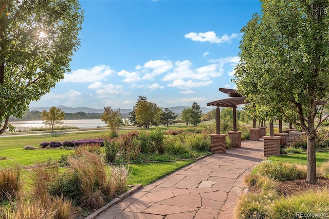 view of property's community with a water and mountain view, a pergola, and a lawn