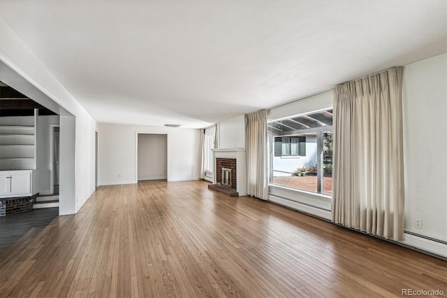 unfurnished living room with wood-type flooring, a baseboard heating unit, and a brick fireplace