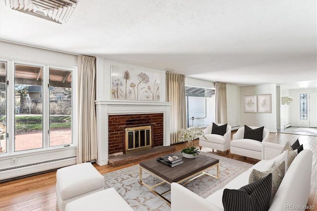 living room with baseboard heating, light wood-type flooring, and a brick fireplace